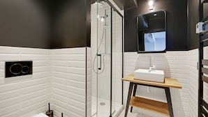 A modern bathroom with a glass-enclosed shower, a white sink with a wooden shelf, and a black-framed mirror. - Superb Family Apartment - 1 Bedroom (Paris)