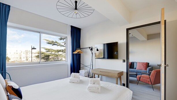 A hotel room with a large bed, a desk, a chair, a TV, and a view of the city. - Superb Family Apartment - 1 Bedroom (Paris)