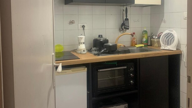 Eine kleine Küche mit Kühlschrank, Backofen und einem kleinen Tresen mit Wasserkocher und Ventilator.