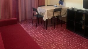 Ein kleines Zimmer mit einem roten Sofa, einem Esstisch mit Stühlen, einem Fernseher auf einem Schrank und einem Bild des Eiffelturms an der Wand.