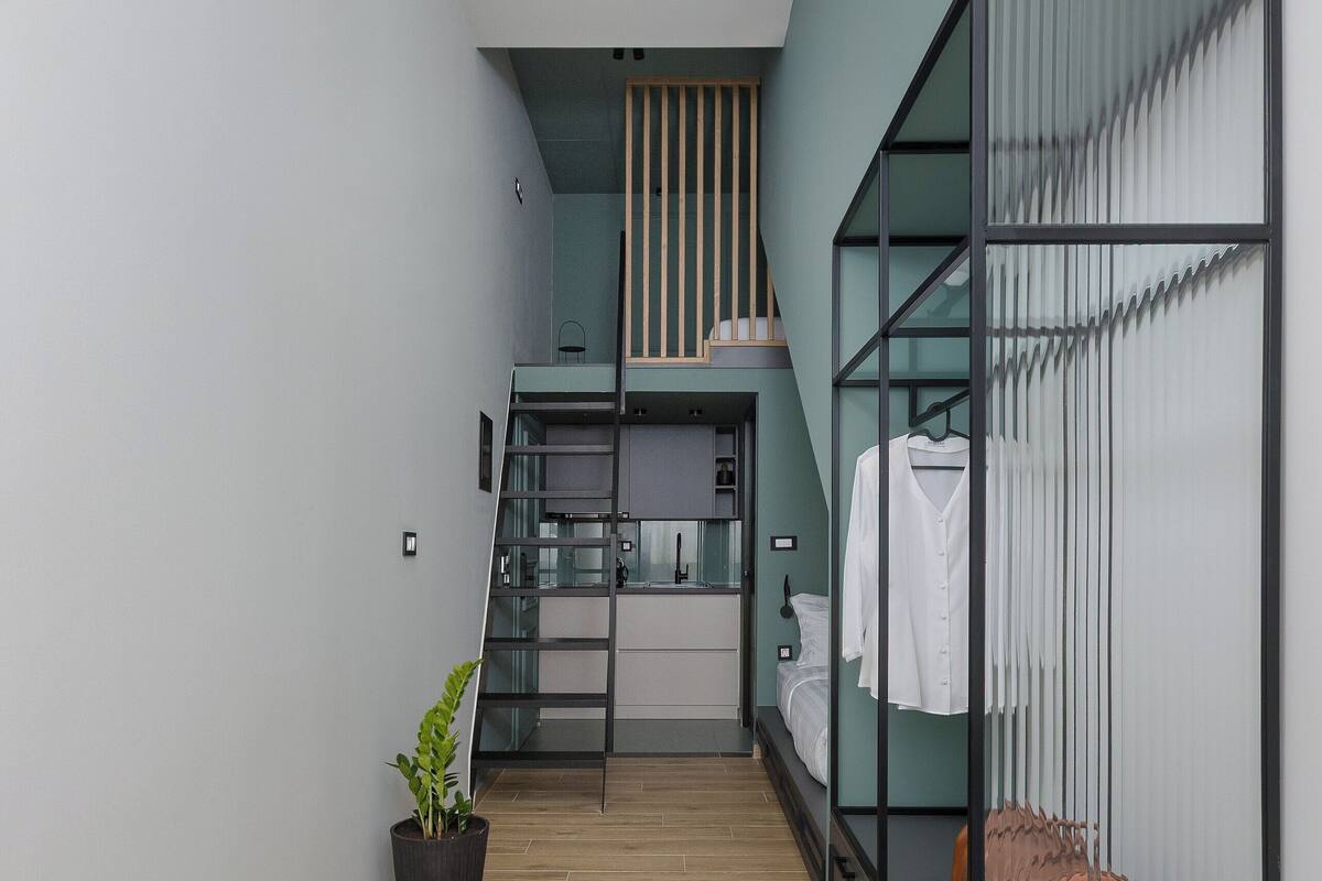 A modern, compact room with a loft bed, a small kitchenette, and a potted plant.