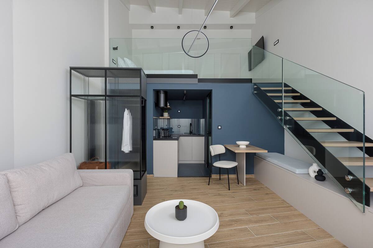 A modern living space with a sofa, a dining area, a kitchen, and a staircase.