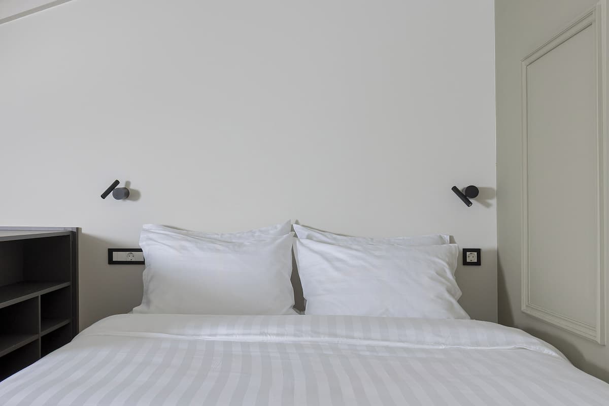 A neatly made bed with white linens and pillows, a bedside shelf, and two wall-mounted nightstands with lamps.
