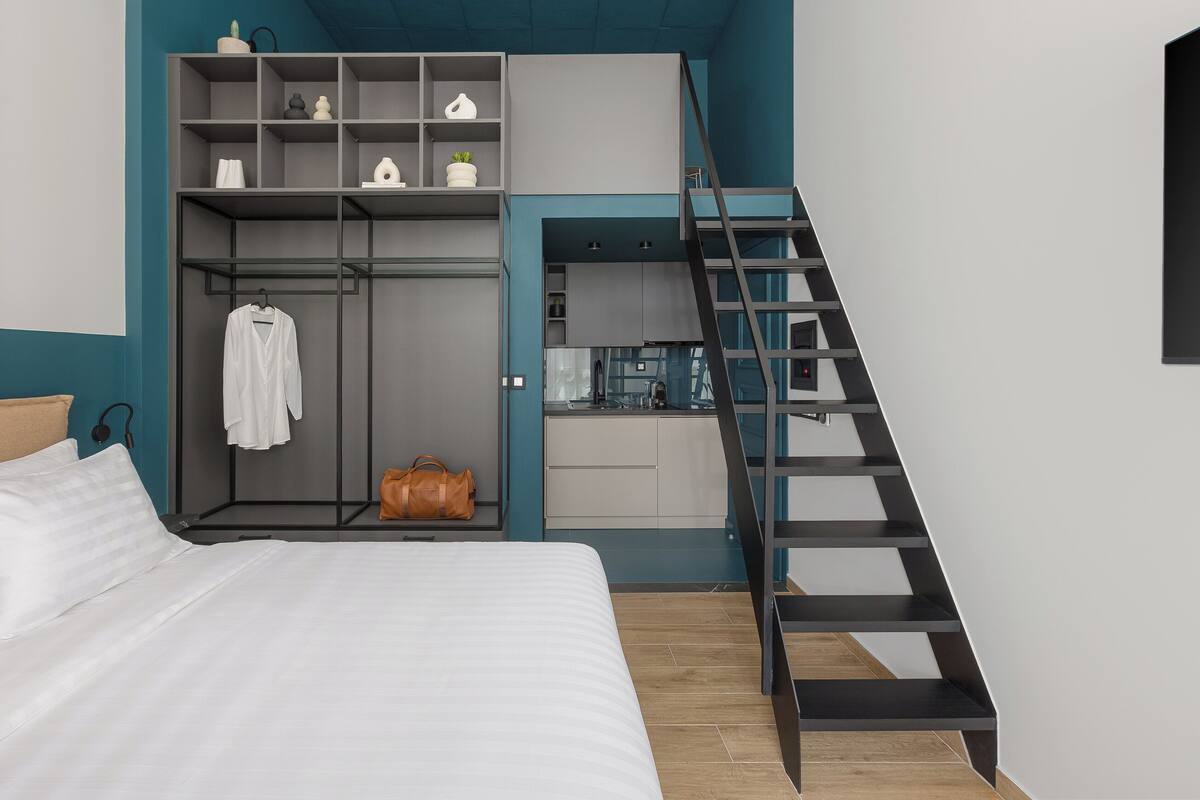 A bedroom with a bed, a wardrobe, a small kitchenette, and a staircase.