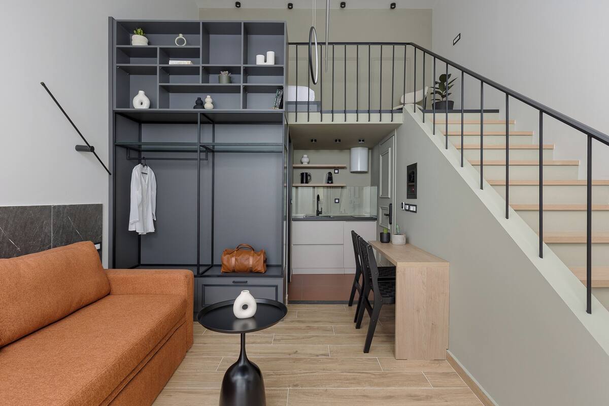 A modern living room with a sofa, a table, a staircase, and a kitchen area.