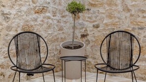 Due sedie in metallo nero, un tavolino e una pianta in vaso, tutto addossato a un muro in pietra.