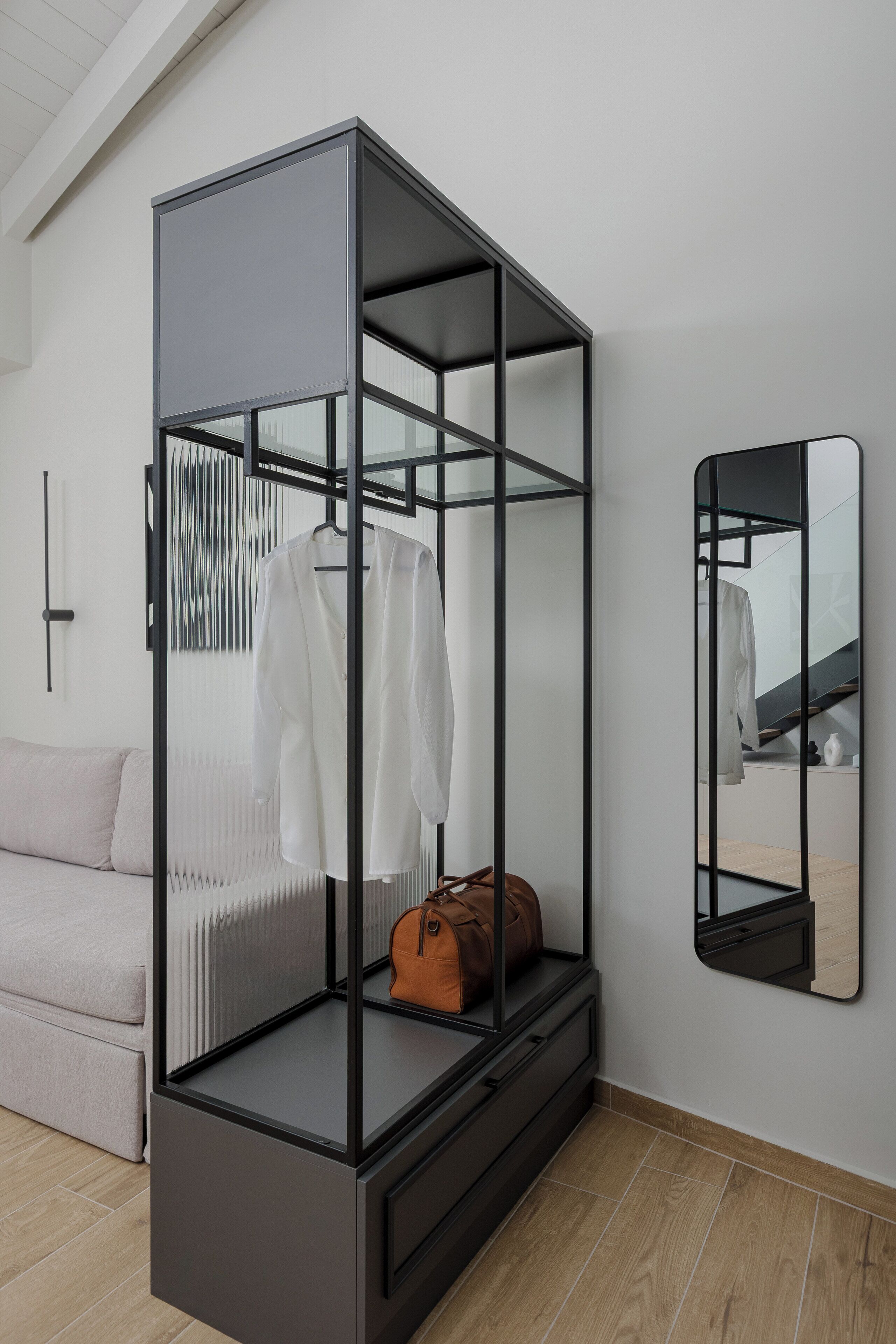 Ein modernes Zimmer mit einem raumhohen Glas-Kleiderschrank, einem Spiegel und einer Couch.