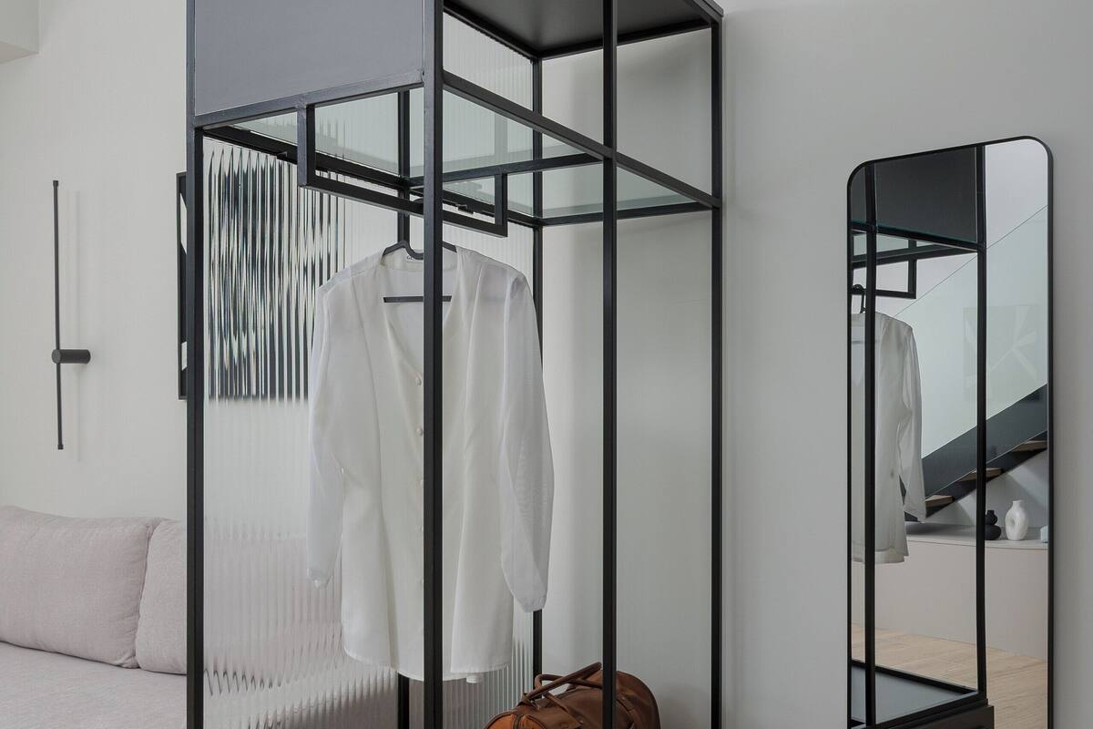 A modern room with a glass partitioned wardrobe, a mirror, and a sofa.