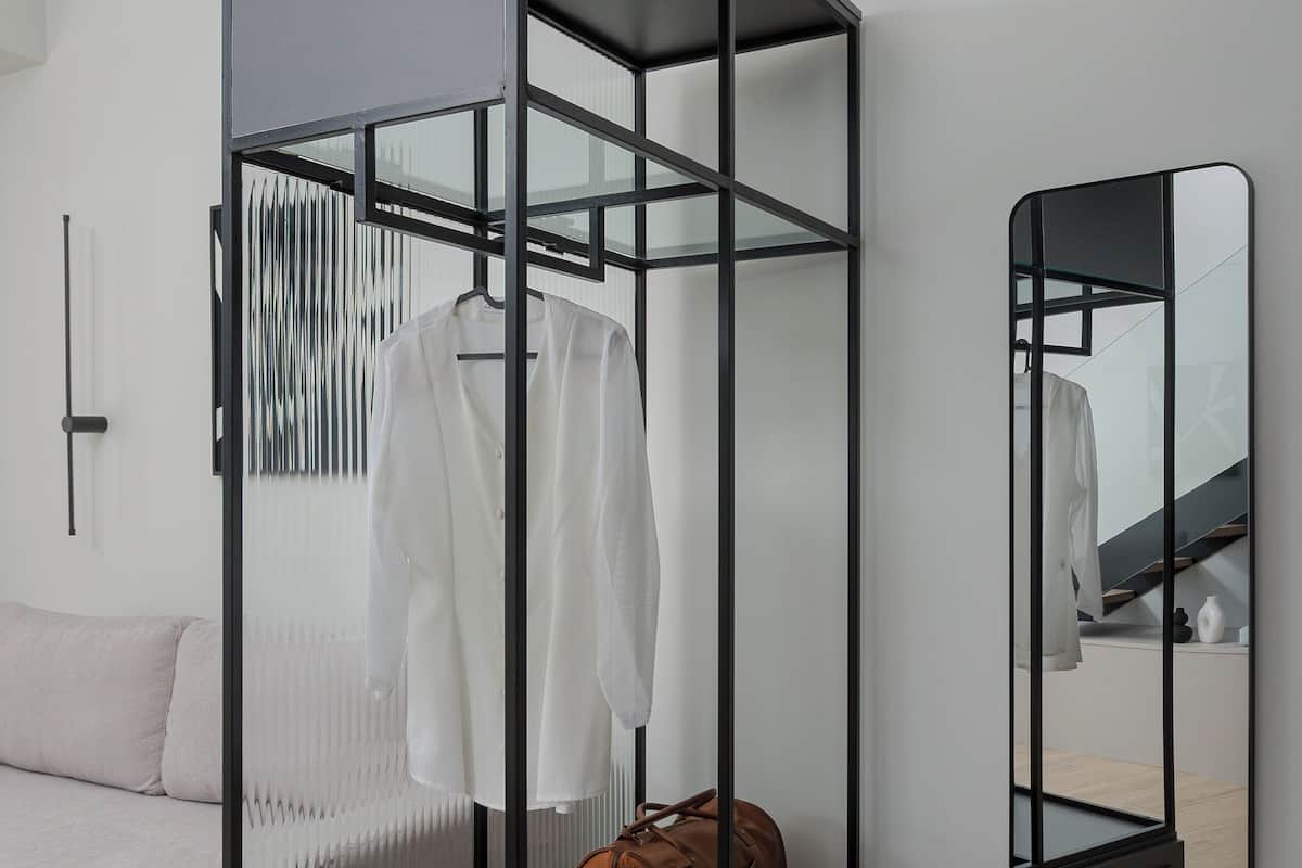 A modern room with a glass partitioned wardrobe, a mirror, and a sofa.