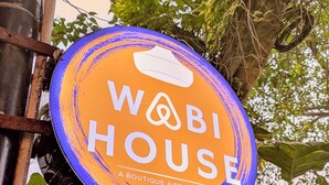 WABI HOUSE -niminen, tyylikkäänä Airbnb-majoituspaikkana tunnettu kohde, jonka kyltti on kiinnitetty metalliseen tolppaan. Taustalla on vehreää kasvillisuutta ja näkyvissä on kivirakennelma.