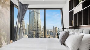 Una habitación de hotel moderna con una cama grande, vistas a un horizonte urbano y un amplio ventanal con cortinas.