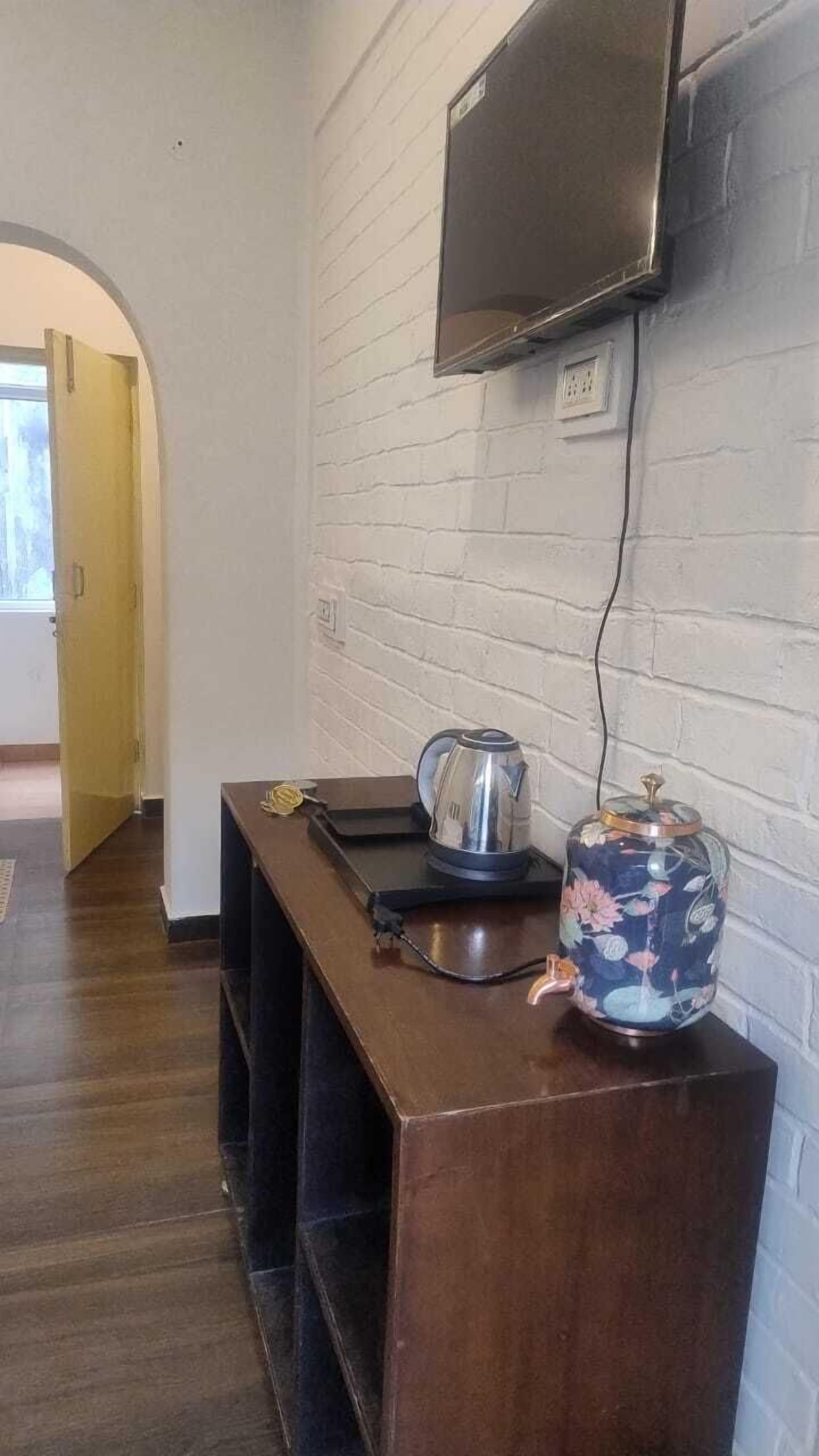 Ein Zimmer mit einer hölzernen Bank, einem Wasserkocher, einer Teekanne und einem an einer weißen Ziegelwand befestigten Fernseher.