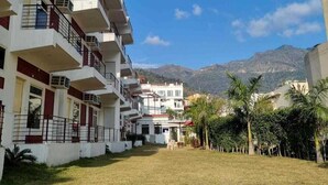 A multi-story residential building with balconies, a grassy courtyard, and a mountainous backdrop. - Hotel Aviral Ganga (Rishikesh)