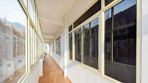 A corridor with large windows, a tiled floor, and a view of a building outside. - Hotel Aviral Ganga (Rishikesh)