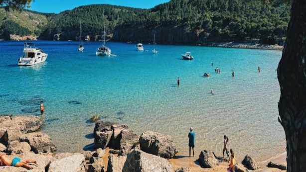 A coastal scene with clear turquoise water, rocky shoreline, and boats. - Casa Quatre Brises (L'Escala)