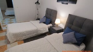 Quarto de hotel com duas camas, uma mesinha de cabeceira com abajur e uma obra de arte na parede.