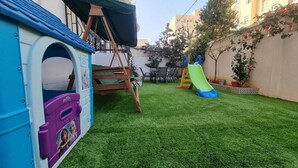 Uma área de recreação infantil com escorrega, uma pequena estrutura de escalada e um casebre.