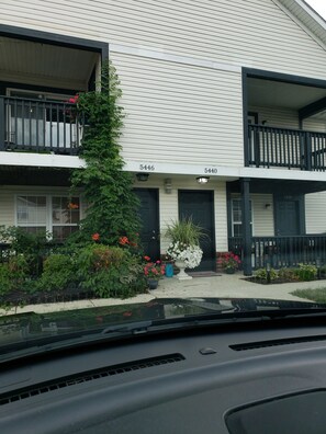 A two-story building with numbered doors, a small garden with various plants and flowers, and a visible balcony. - 5 HOSPITALS WITHIN 1O MILE RADIOUS Luxurious 1Bed EXTRA PLUSH! NO PET FEES! (Columbus)