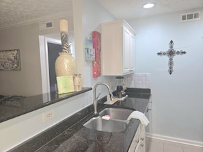 A kitchen with a black countertop, stainless steel sink, white cabinets, and a decorative cross on the wall. - 5 HOSPITALS WITHIN 1O MILE RADIOUS Luxurious 1Bed EXTRA PLUSH! NO PET FEES! (Columbus)