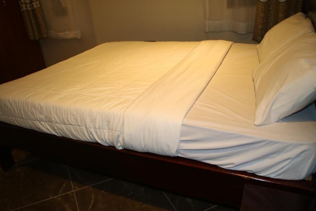 A neatly made bed with white bedding in a room with a tiled floor and a wooden headboard.