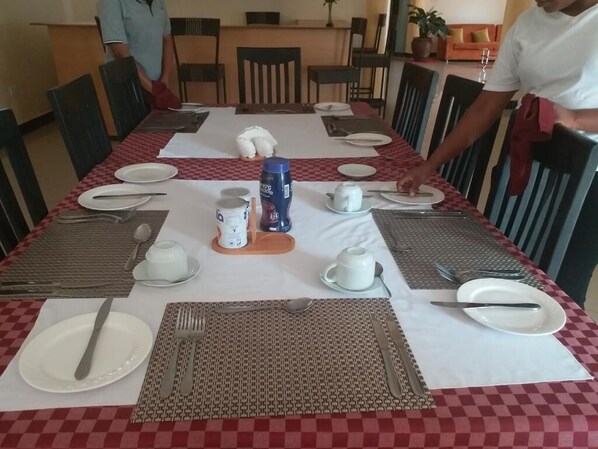 A dining table set with plates, cutlery, and a coffee machine. - Acactus Hotel (Kampala)