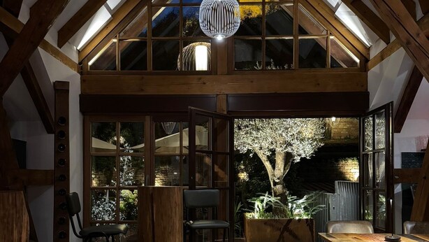 Un loft spacieux avec de hauts plafonds, des poutres en bois et de grandes fenêtres. On y trouve plusieurs coins salon avec des chaises et des tables.