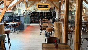 Un restaurant doté d’un haut plafond en bois, de poutres apparentes et d’un mur en pierre. Les tables et les chaises sont disposées pour accueillir les clients.