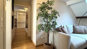 Un salon moderne avec un plancher en bois, un canapé blanc, une plante en pot et un luminaire au plafond.
