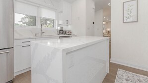A modern kitchen with a large island, white cabinetry, and a view of the living area.