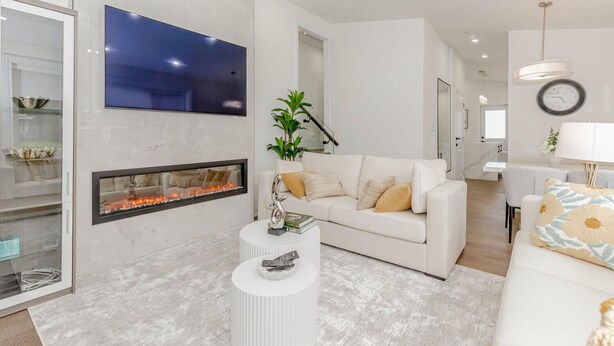 A modern living room with a fireplace, a white sofa, and a flat-screen TV mounted on the wall.