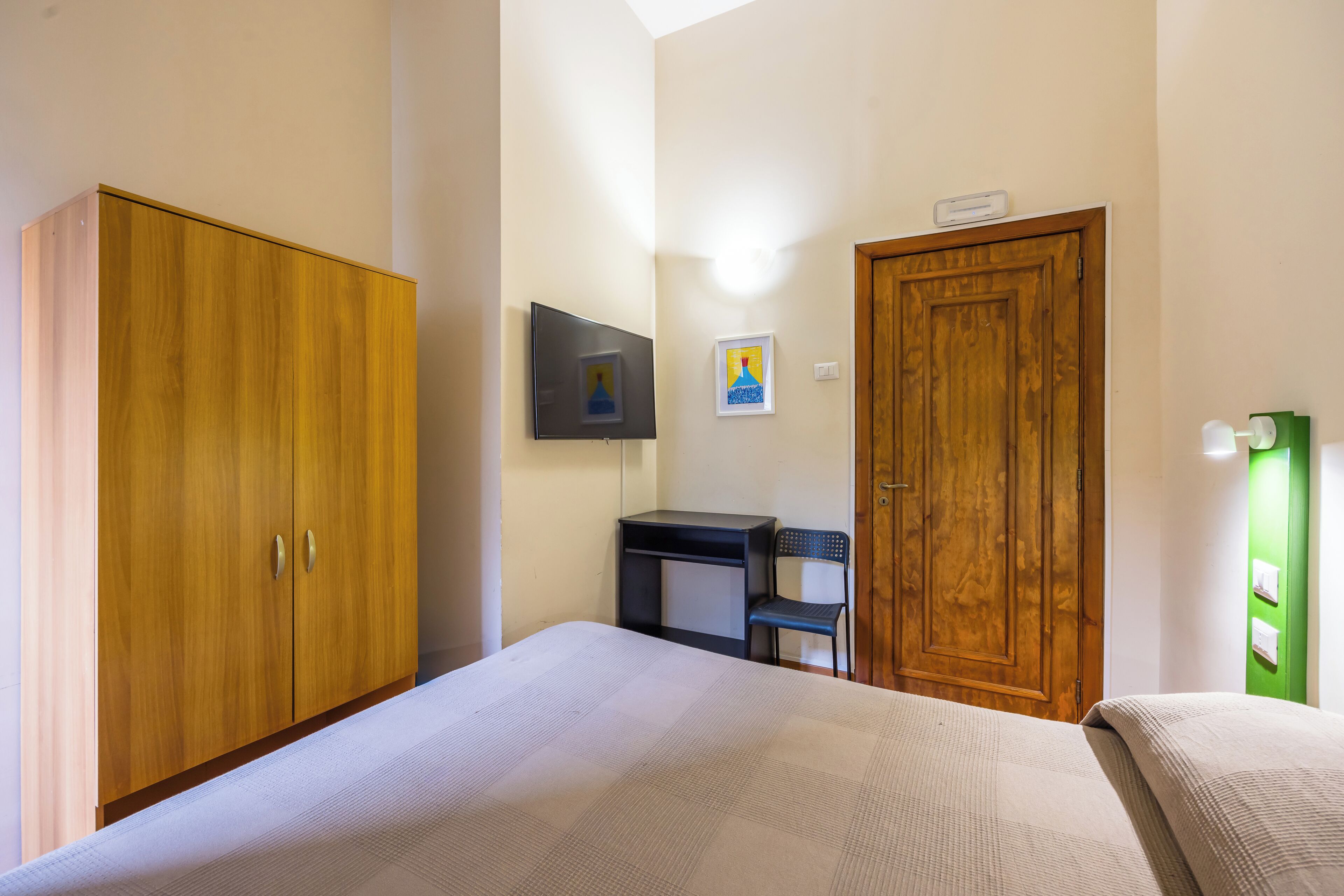 Ein Schlafzimmer mit Bett, Holzschrank, Schreibtisch, Stuhl und einer Tür.