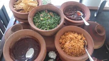 Una mesa con varios platos en cazuelas de barro, incluyendo un guiso verde de verdura, salsa roja y un plato de arroz amarillo.