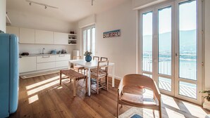 A modern kitchen with white cabinets, a dining table with chairs, and a view through large sliding doors to a balcony. - Infinito (Como)