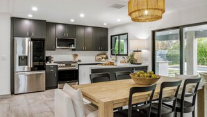 Una cocina moderna con armarios oscuros, electrodomésticos de acero inoxidable y una mesa de comedor de madera.