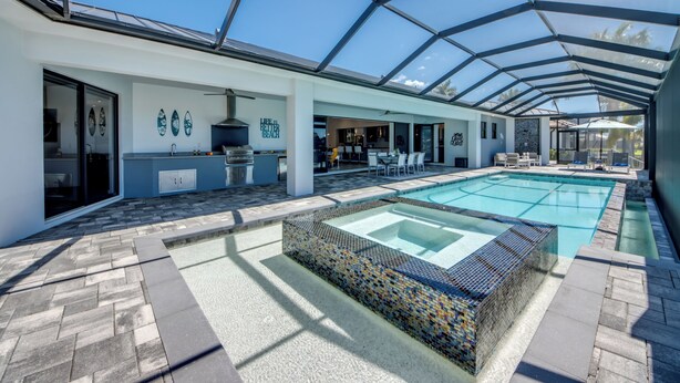 Un área moderna de piscina al aire libre con un porche de cristal, un espacio de descanso y una cocina con parrilla.