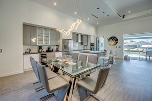 Une cuisine moderne avec une table à manger en verre, des chaises contemporaines et une vue sur l’extérieur.