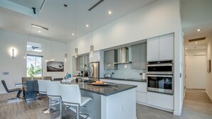 Una cocina moderna con armarios blancos, electrodomésticos de acero inoxidable y una isla central con taburetes de bar.