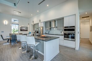 Une cuisine moderne avec des meubles blancs, des appareils en acier inoxydable et un îlot central doté de tabourets de bar.