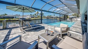 Un espacio al aire libre techado con piscina, sillones de descanso y una mesa con bebidas.