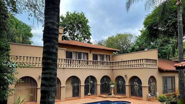 Una casa de dos pisos con piscina, ventanas en arco y un balcón.