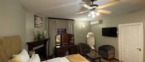 A hotel room with a bed, a desk, a chair, a ceiling fan, an air conditioning unit, a television, and a door.