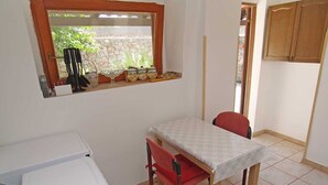 Een kleine keuken met een tafel en stoelen, een raam met planten, en een wasmachine.