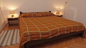 Een net opgemaakt bed met een geborduurde deken, twee bedlampen en een gestreept vloerkleed op een houten vloer.