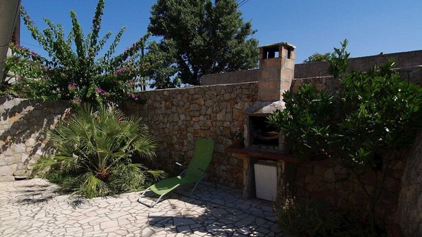 Een terras van natuursteen met een groene lounge stoel, een stenen muur en een klein buitenkeuken.