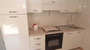Een kleine keuken met witte kastjes, een fornuis, een spoelbak en een waterkoker.