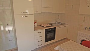 Een kleine keuken met witte kastjes, een inbouwoven, een spoelbak en een wasmachine.