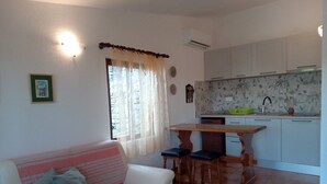 A living room with a sofa and a small dining table with two chairs. There is a kitchen area with white cabinets and a sink. - Ercilia house / Ercilia A2 (Veli Lošinj)