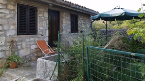 A stone house with a tiled roof, a door, and windows with shutters. There is a chair and a potted plant outside. - Ercilia house / Ercilia A2 (Veli Lošinj)