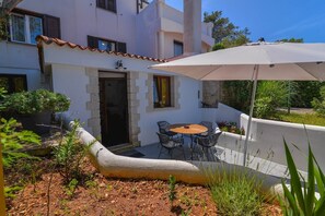 Eine Terrasse mit Tisch und Stühlen, umgeben von Blumentöpfen und einer weißen Mauer.