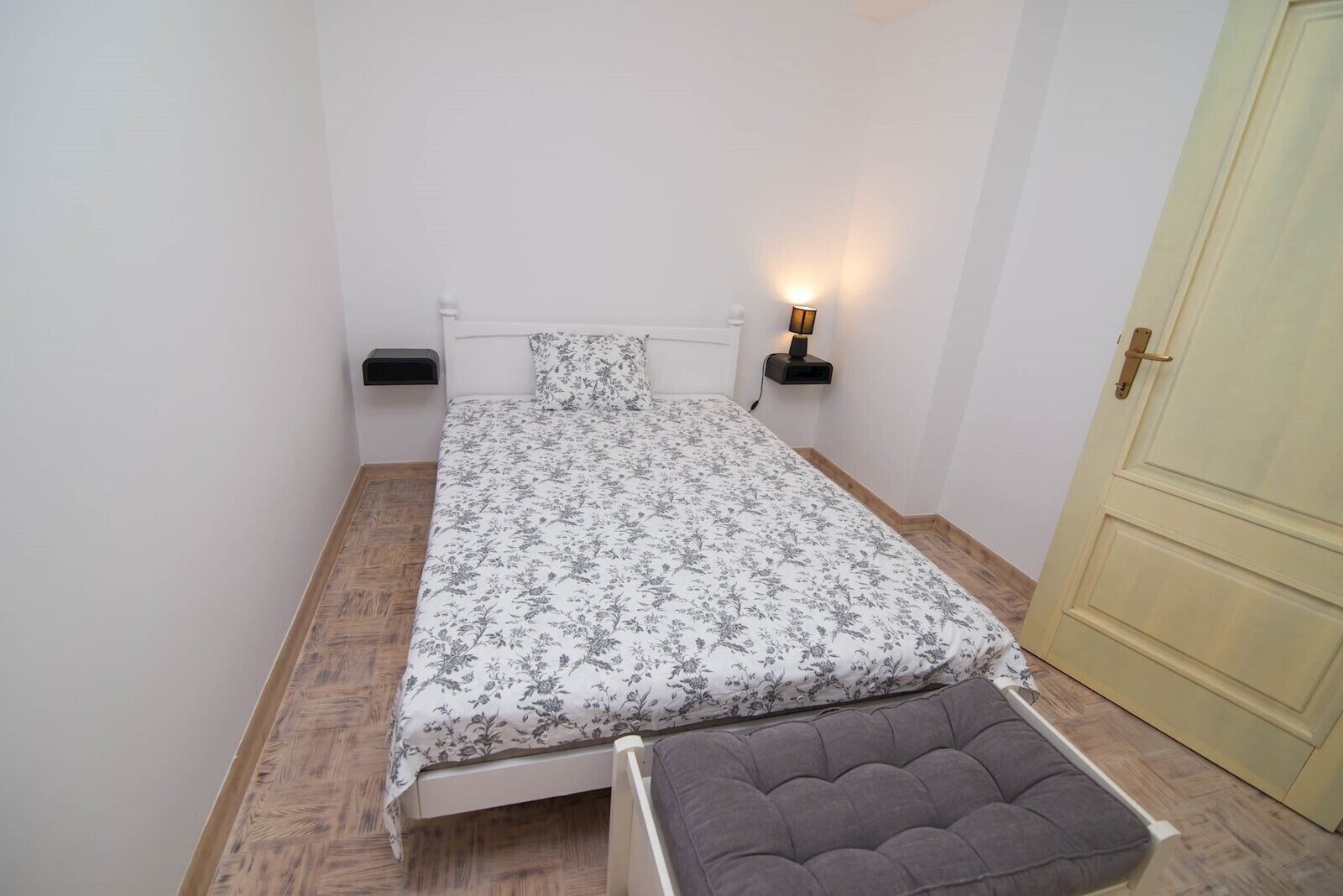 Ein kleines, aufgeräumtes Schlafzimmer mit einem Einzelbett, Nachttischen und einer Tür.